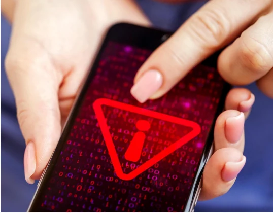 Hands holding a smartphone displaying a red alert warning icon